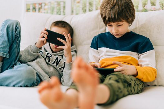 Cheerful two brothers boys playing online game, watching video on cellphone. Smiling kids using funny mobile apps, enjoying free leisure time at home on couch. Children texting together at phone.