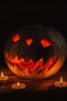 Jack O' Lantern Glowing In Fantasy Night. Halloween. candles are burning nearby. On old wooden background. dramatic frame. vertical orientation.