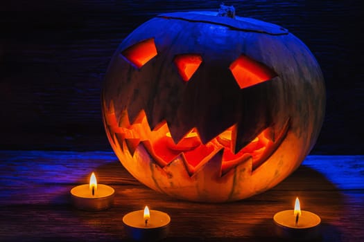 Jack O' Lantern Glowing In Fantasy Night. Halloween. candles are burning nearby. On old wooden background. dramatic frame. horizontal orientation