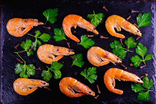 boiled shrimps lie on a slate board along with herbs. top view flat lay.