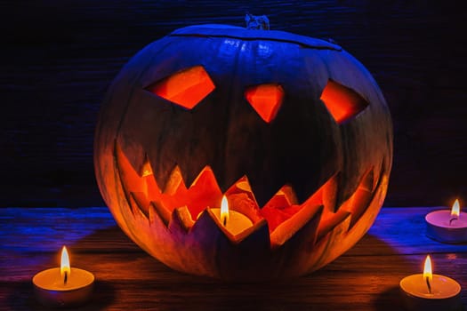 Jack O' Lantern Glowing In Fantasy Night. Halloween. candles are burning nearby. On old wooden background. dramatic frame. horizontal orientation