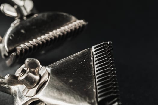 On a black surface are old barber tools.Two vintage manual hair clipper. black monochrome. Close-up. Barbershop background. contrast shadows. Horizontal orientation