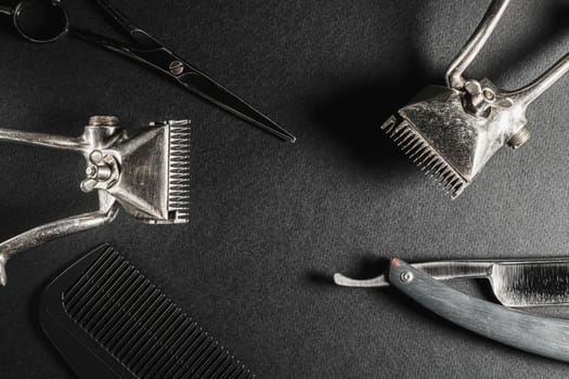 On a black surface are old barber tools. two vintage manual hair clipper, comb, razor, hairdressing scissors. black monochrome. Close-up. Barbershop background. horizontal orientation. Top view, flat lay.