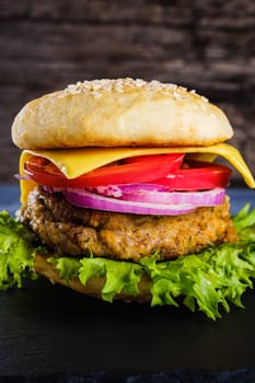 Fresh delicious homemade veggie burger lies on natural slate on rustic wooden background. Delicious tasty burger with lettuce, cheese, onion and tomato. buckwheat and lentil cutlet. Vertical orintation.