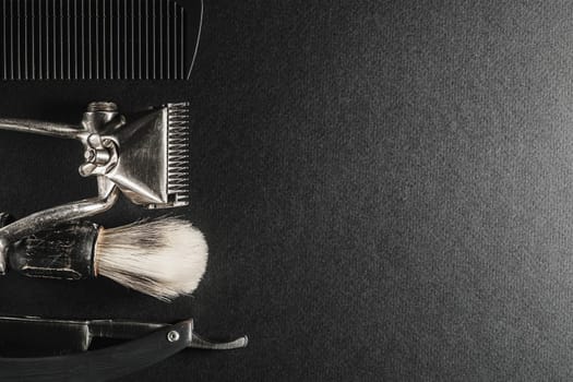 On a black surface are old barber tools.Two vintage manual hair clipper, comb, razor, shaving brush, hairdressing scissors. black monochrome. Close-up. Barbershop background. contrast shadows. Horizontal orientation. Top view, flat lay. copy space