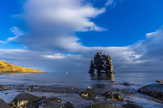 Blurred tourist approaching to Hvitserkur dragon drinking boulder, long exposure in Iceland