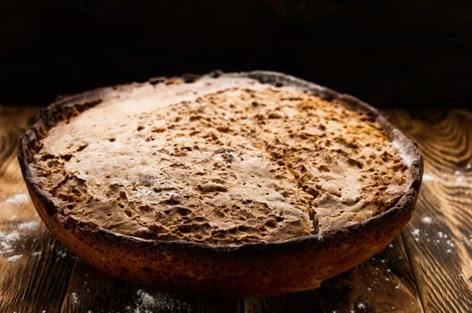 big whole handmade round black bread with interesting texture lie on dark wooden table