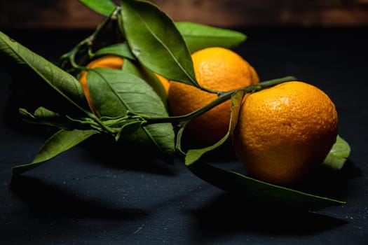 on a dark surface are three tangerines with leaves. Horizontal orientation.