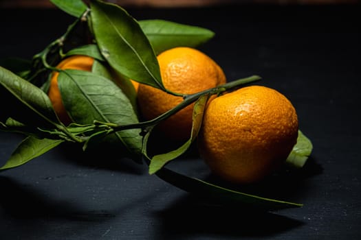 on a dark surface are three tangerines with leaves. Horizontal orientation.