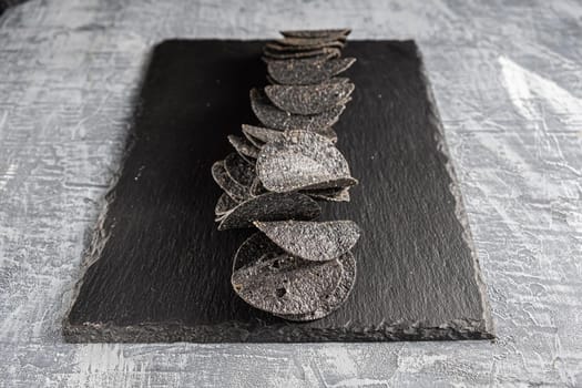 a lot of black chips with spices on a slate dish that lies on a concrete texture.