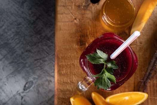 smoothie consists of beetroot pumpkin, orange, celery in mason jar. smoothies are poured in layers. next to it is a jar of honey, beet root, a piece of pumpkin and slices of orange. on a thick wooden board. horizontal orientation.