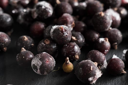 Organic natural frozen blackcurrant berries covered with hoarfrost scattered on a slate dish. Horizontal orientation. Close-up.