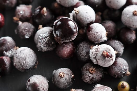 Organic natural frozen blackcurrant berries covered with hoarfrost scattered on a slate dish. Horizontal orientation. Close-up.