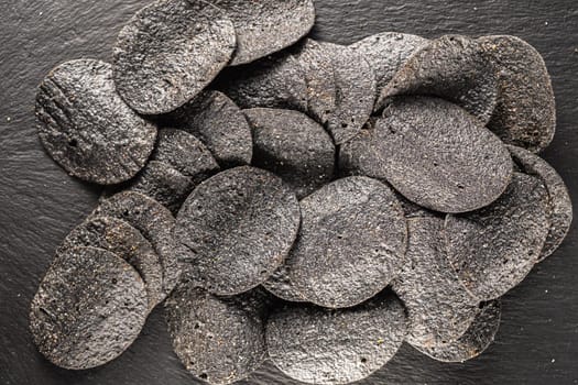 background of many black chips with spices on a slate dish. close-up.