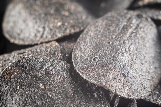 background of many black chips with spices on a slate dish. close-up.