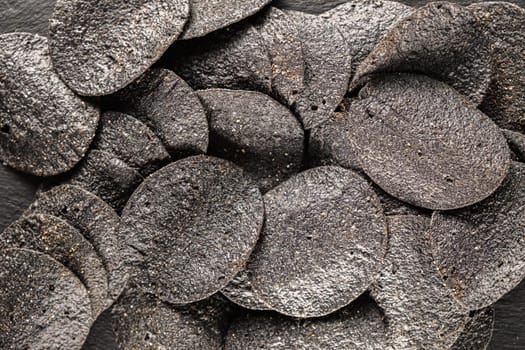 background of many black chips with spices on a slate dish. close-up.