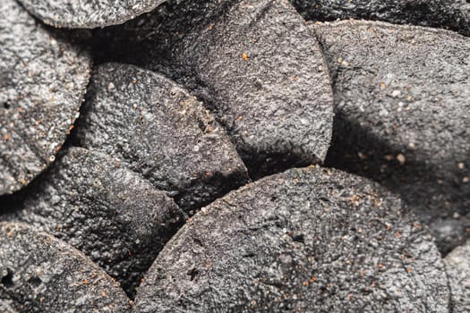 background of many black chips with spices on a slate dish. close-up.