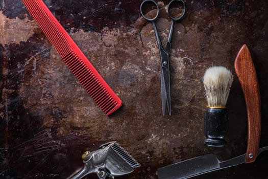Old barber tools on an old beautiful rusty surface. A razor, shaving brush, comb, hairdressers scissors, and a clipper. horizontal orientation. copy space. dark photo. flat lay. top view.