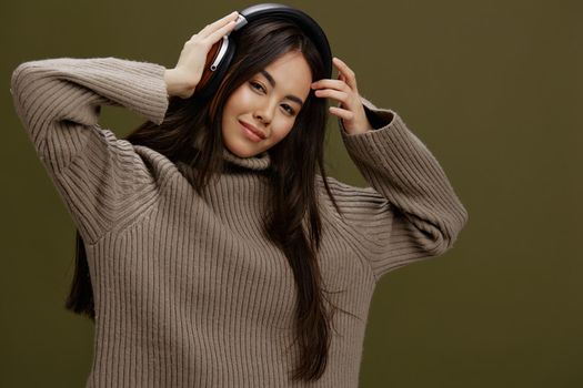 young woman in a sweater listening to music with headphones fun Green background. High quality photo