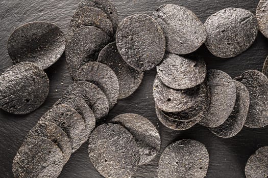 background of many black chips with spices on a slate dish. close-up.