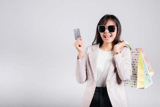 Woman with glasses confident shopper smile hold online shopping bags and credit card for payment on hand, Portrait excited happy Asian female fashion shop studio shot isolated on white background