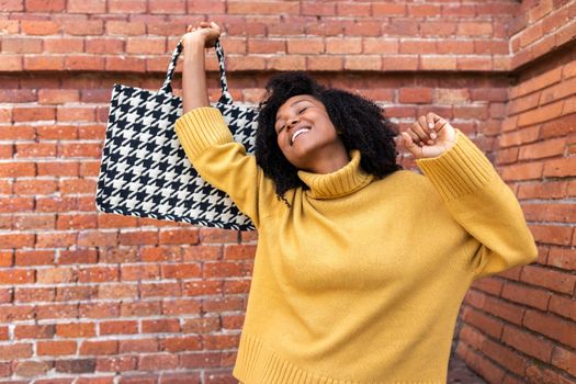 Joyful young african american woman dancing holding her handbag. Happiness and lifestyle concept.