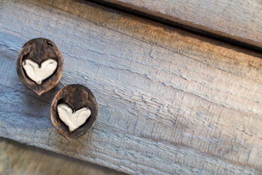 Two halves of split walnut with core in form of white hearts on wooden background, diagonal lines. Concept of Valentine's Day and health. Copy space.