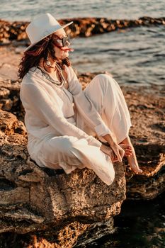 A woman in a white pantsuit and hat is standing on the beach enjoying the sea. Happy summer holidays.