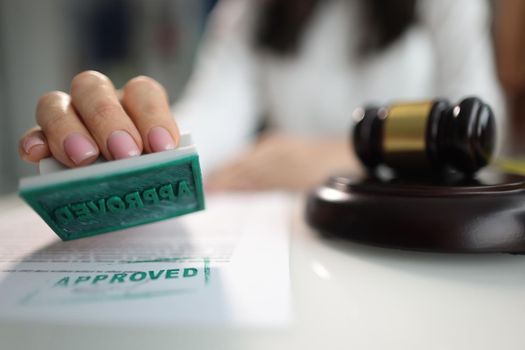 A hand with a stamp approved near the judge's gavel, close-up. Legislative project, justice in court, jurisprudence