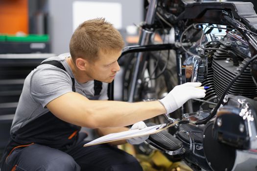 A man in uniform sits in a workshop near a motorcycle, close-up. Motorbike check before the race, motorcycle club