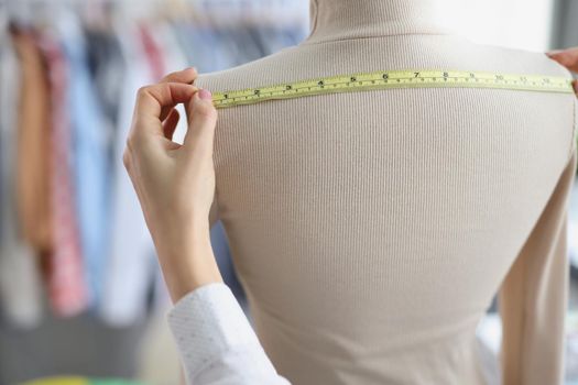 Hands of a seamstress with a measuring tape measures on a mannequin, close-up. Design studio, fashion house