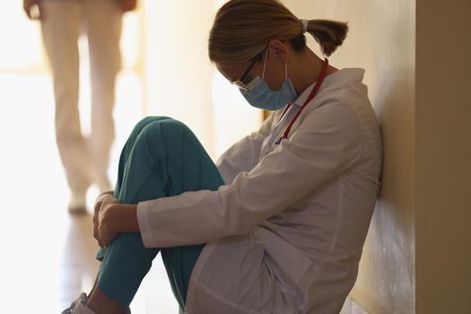 A female doctor sits on the floor with her head bent, close-up. Pandemic fatigue, burnout of medical staff