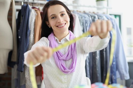 Designer, seamstress in the atelier shows a measuring tape, close-up, blurry. Designing and creating outfits