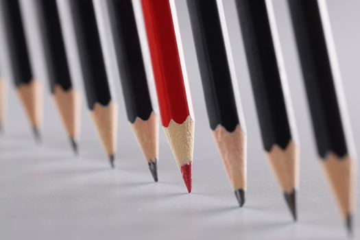 Sharp pencils in a row on a gray background, close-up. Black and red wooden pencils