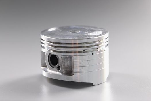 Close-up of a shiny car piston on a gray background. Automotive components, replacement and repair