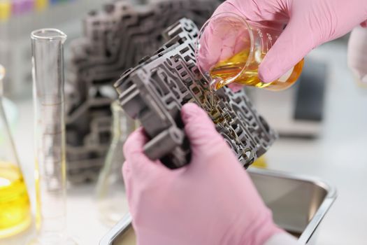 Hands in the laboratory pour oil on the gearbox, close-up. Car oil test, car parts cleaning, chemical testing