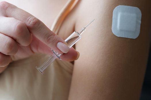 Fingers with a filled syringe near his shoulder, close-up. Insulin injection, intramuscular vitamin intake