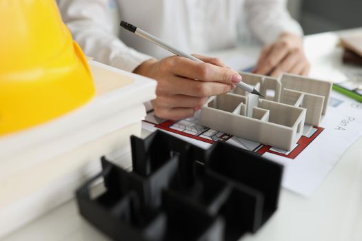 The architect holds a pen over layout and plan building, close-up. Coordination of house design, documentation