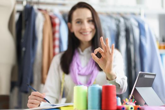 Clothing designer, seamstress in atelier shows ok gesture, close-up, blurry. Search for an artistic image clothing model