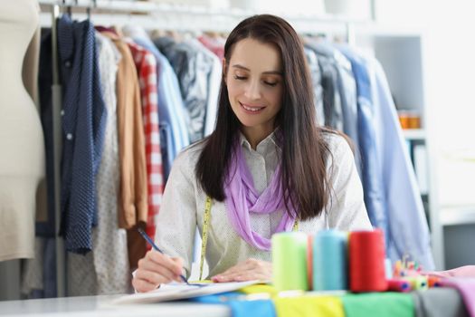 A seamstress in an atelier makes notes, close-up, blurry. Modeling and design of clothing details, clothing designer