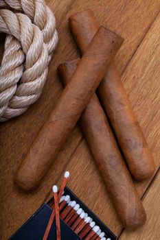 Three cigars, matches and a nautical rope on a wooden table.