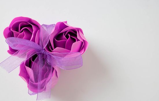 Three pink soap roses tied with a lilac ribbon on a white background. Space for text.