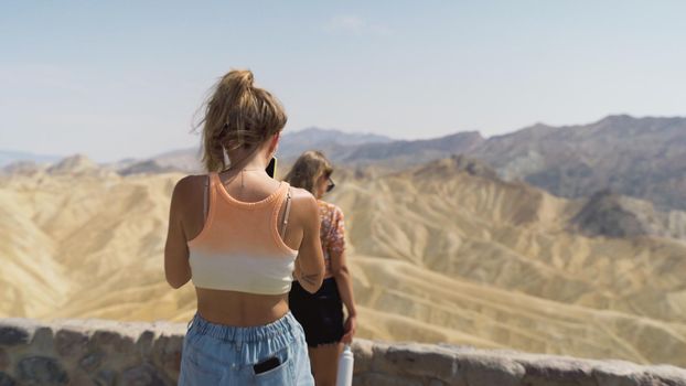 Lovable caucasian girls expressing positive emotions to camera. Outdoor photo of refined sisters posing against background with mountains in the Mojave Desert