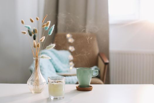 Cup of coffee and a transparent vase with dried flowers at white background. 