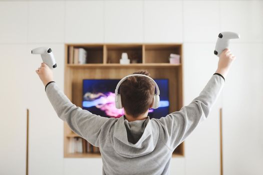 Boy in headphones watching television, teenager boy playing video game in front of screen at home.