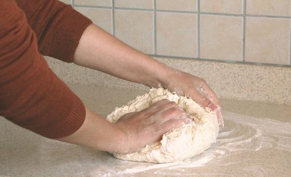 woman hands knead the yeast dough for pizza and bread. there is a flour around it on kitchen table