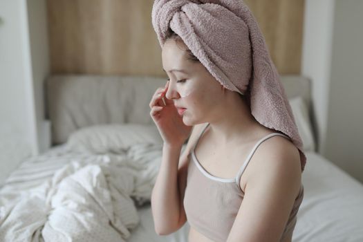 smiling young woman with a towel on head apply cream on face skin