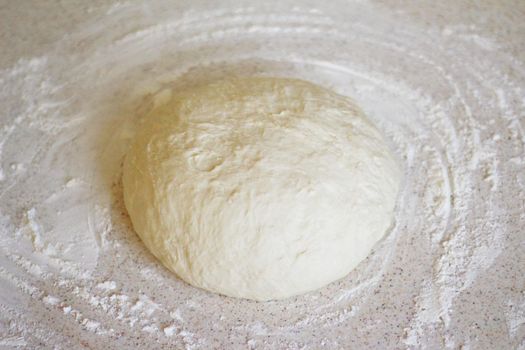 a yeast dough for pizza and bread is on kitchen table. there is a flour around it. the dough is waiting for its time to be baked