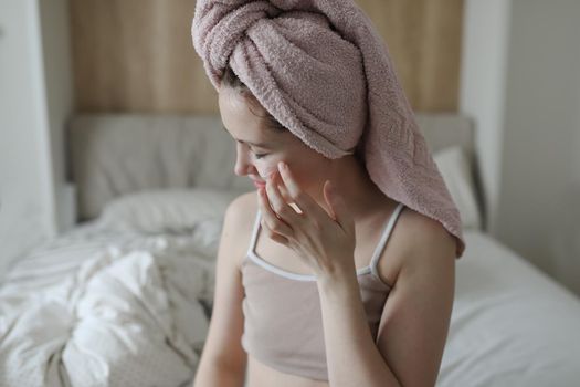 smiling young woman with a towel on head apply cream on face skin