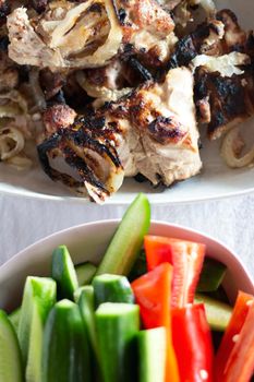 barbecue meat with fresh vegetables are in white plates on white table. chicken meat, cucumbers and red sweet pepper